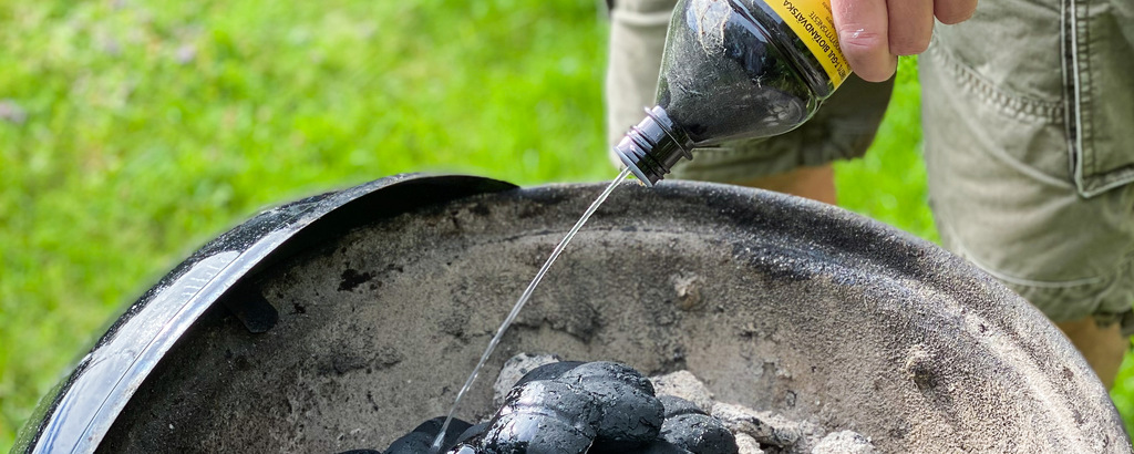 Man häller tändvätska på kolen i en grill.