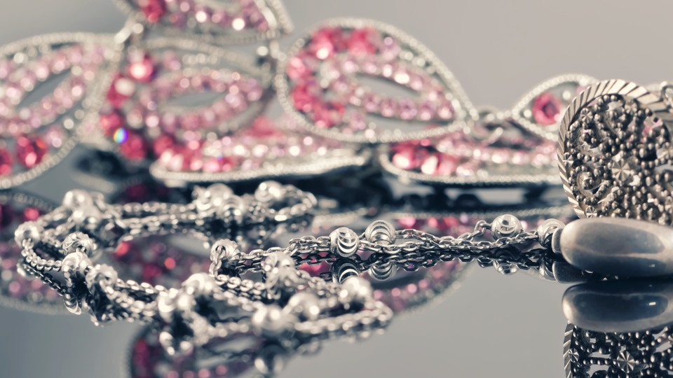 Silversmycken och i bakgrunden ett smycke med röda och rosa stenar