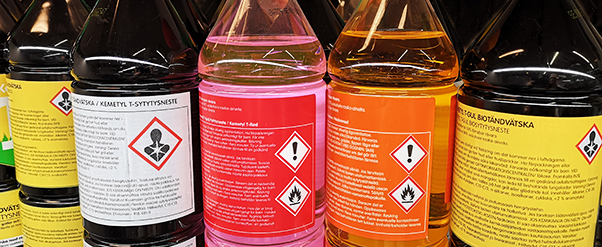 Plastflaskor med olika kemiska produkter i form av vätskor, synliga farosymboler på etiketterna.