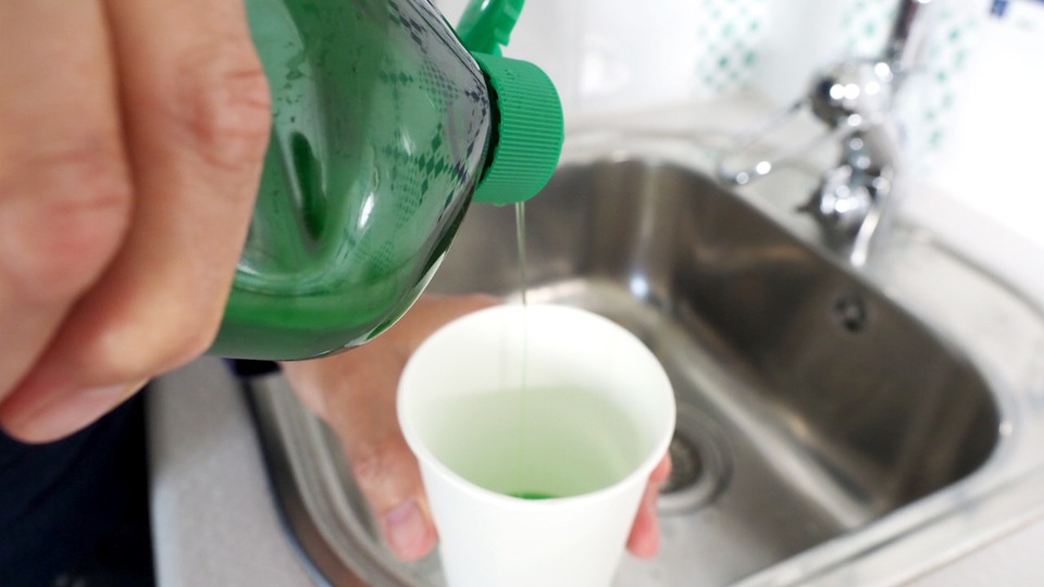 A person is pouring fairy liquid into a cup.