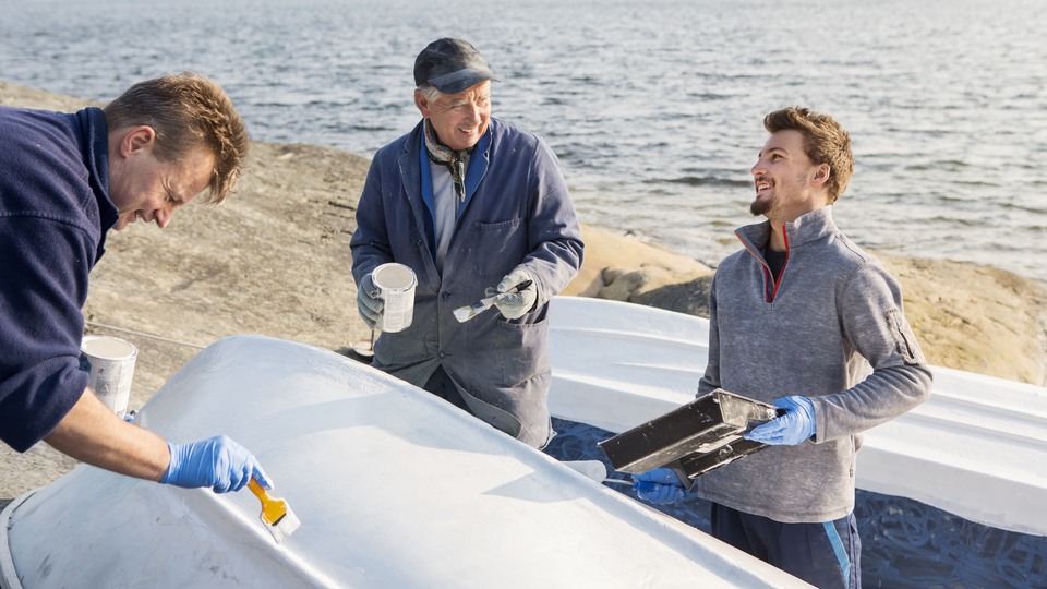 Tre män som målar botten på en båt.