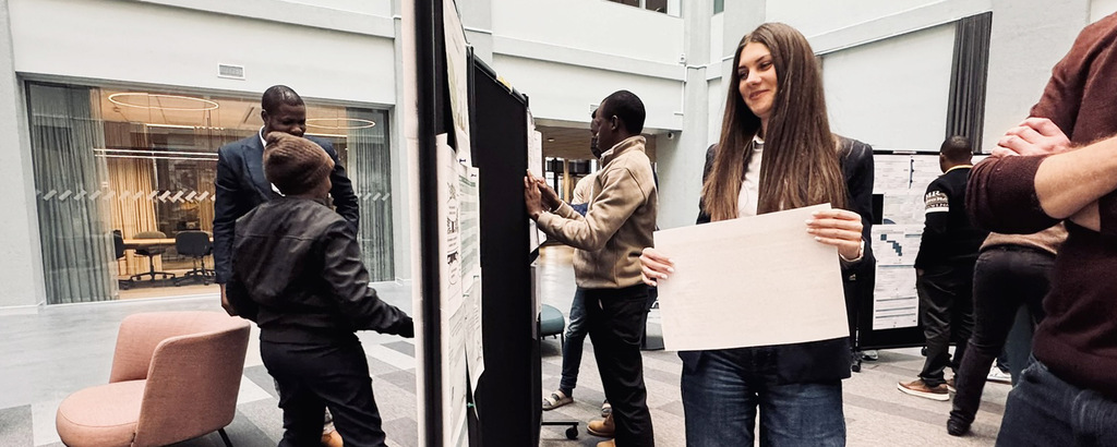 A smiling woman with long dark hair walks towars a posterwall with her poster.
