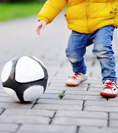 Ett barn som leker med en fotboll på en asfalterad gata.