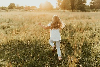A girl runnicng on a meadow, hunting soap bubbles.
