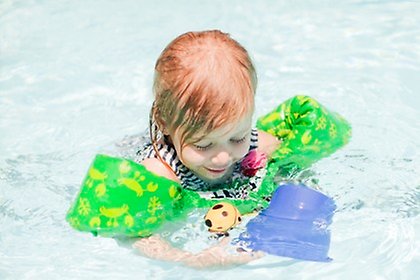 Ett barn med simpuffar på armarna som leker med plastleksaker i en pool.